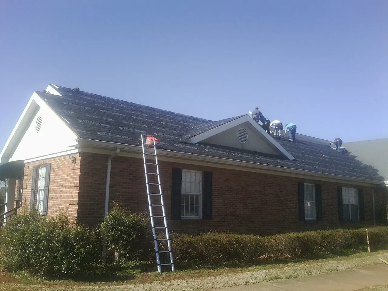 Crew tearing shingles off a brick ranch roof with a ladder set — Metal Roof Repair work by our crew in Rohnert Park