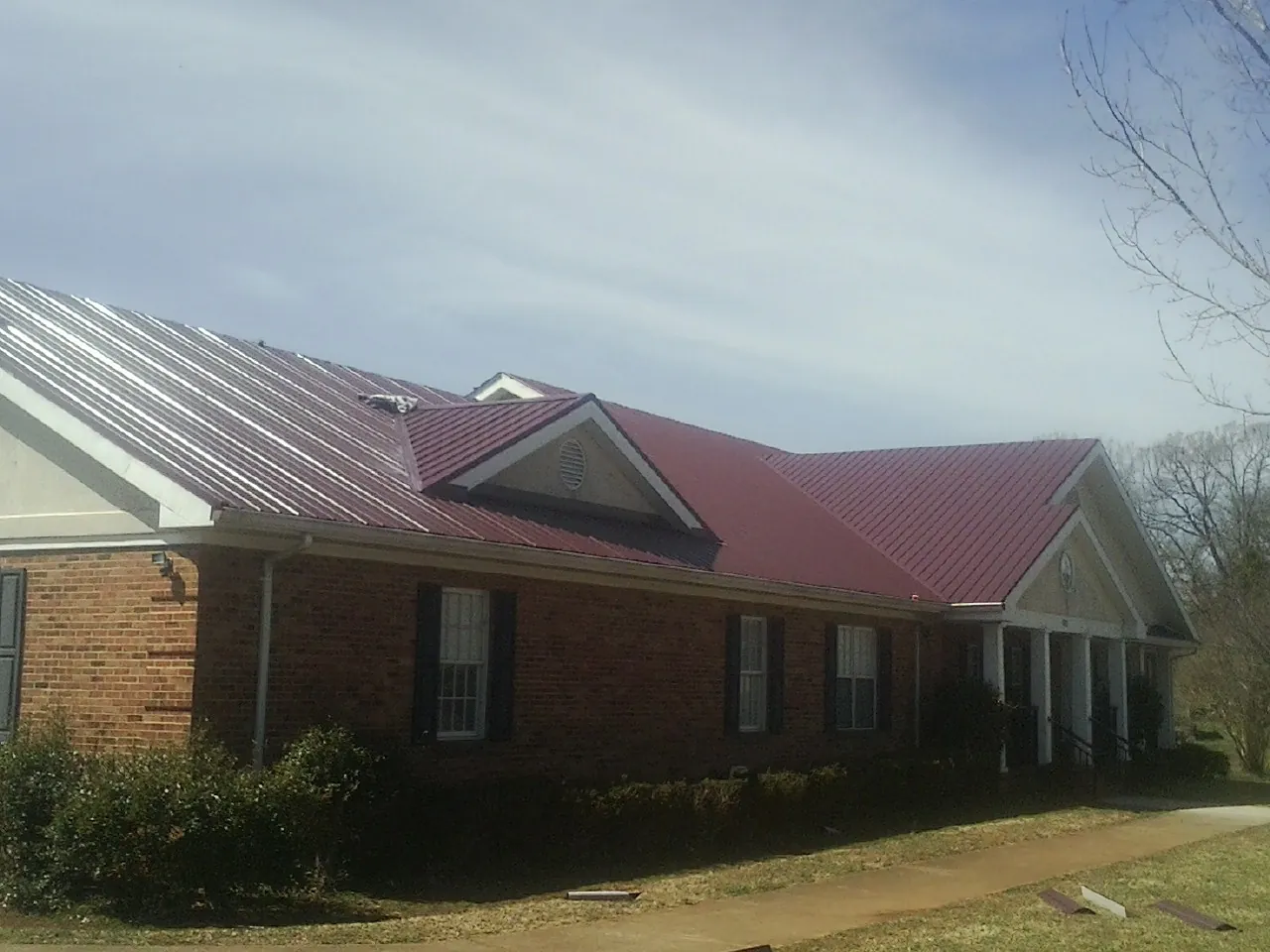 Red metal roof with gabled entries on a long brick building, from a Hail Damage Roof Repair job in Rohnert Park