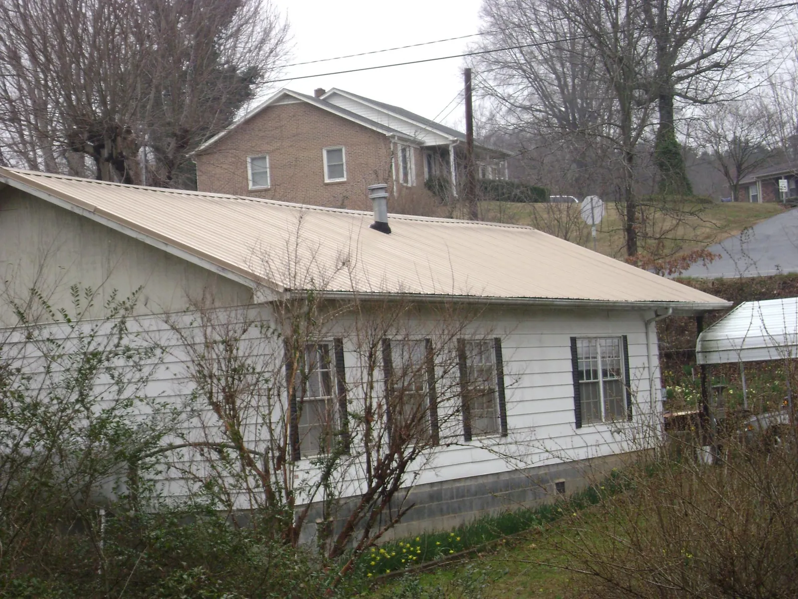 Tan metal roof on a white sided house set into a hillside — Commercial Roofing by Roofing Brothers in Rohnert Park